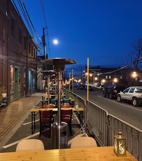 Outdoor dining area with heaters, tables, and chairs, set against a twilight street scene.