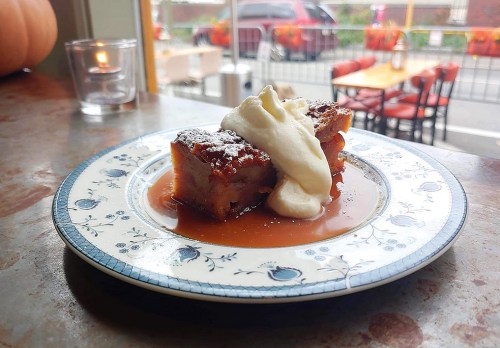 A slice of dessert topped with whipped cream and powdered sugar, served on a decorative plate with caramel sauce.
