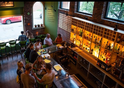 A lively bar scene with patrons enjoying drinks and food, surrounded by brick walls and warm lighting.