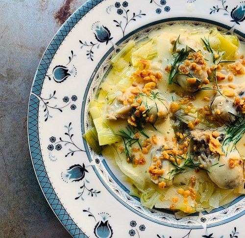 A plate of creamy leeks topped with herbs and crunchy bits, served on a decorative blue and white patterned dish.