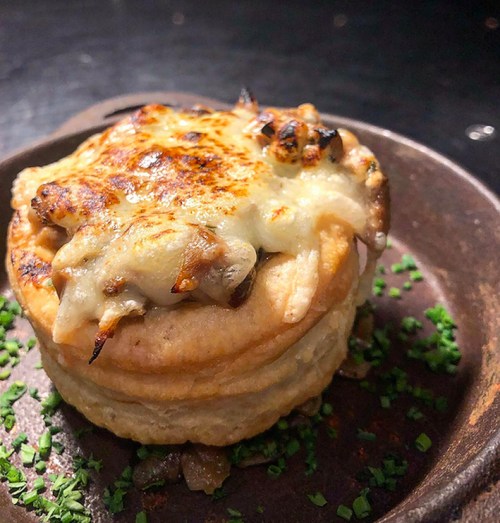 A golden-brown pastry filled with cheese and mushrooms, served on a rustic plate with chopped herbs.