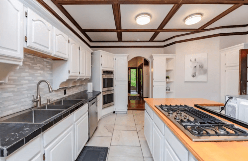 Bright kitchen with white cabinets, a black countertop, and a gas stove, featuring a coffered ceiling and an archway.