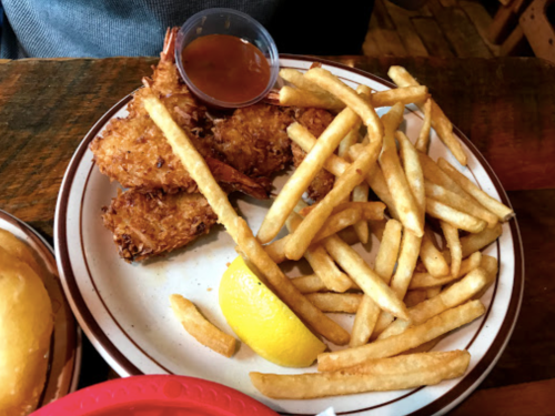 A plate with crispy fried shrimp, a side of French fries, a lemon wedge, and a small cup of dipping sauce.
