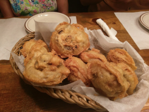 A basket of golden-brown fried snacks, crispy and flaky, served on a table with white napkins.