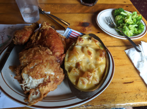 A plate of fried chicken with cheesy potatoes and a side of broccoli on a wooden table.