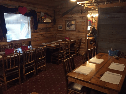 Cozy wooden restaurant interior with rustic tables, chairs, and a window, creating a warm, inviting atmosphere.