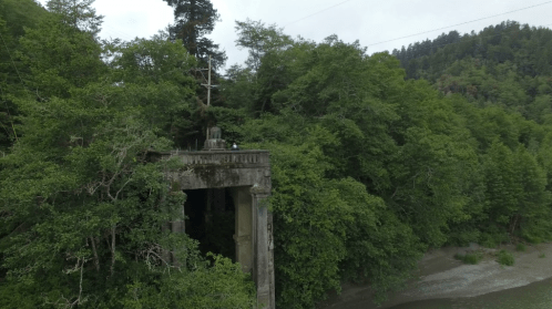 Aerial view of a weathered concrete structure surrounded by dense green trees near a riverbank.