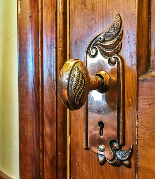 Close-up of an ornate brass door knob and plate on a wooden door, featuring decorative leaf patterns.