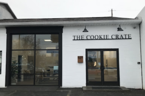 Exterior of "The Cookie Crate" shop, featuring large windows and a modern design on a cloudy day.