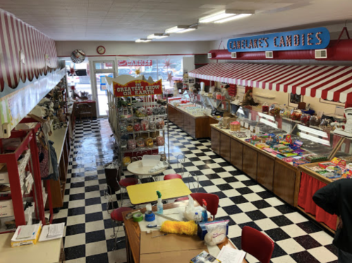 A colorful candy shop interior with checkered floors, display cases, and a bright sign reading "Camelake's Candies."