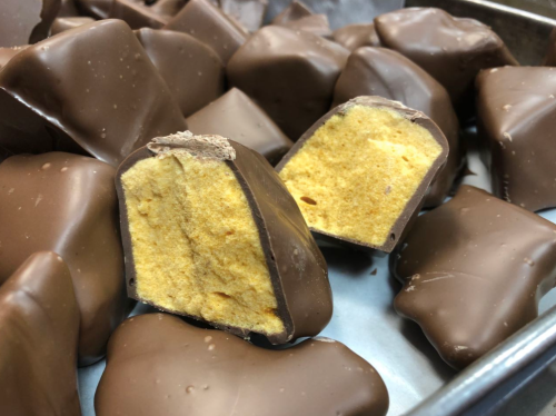 Close-up of chocolate-covered treats, with one cut in half to reveal a yellow, fluffy filling inside.