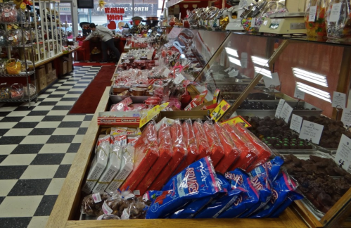 A colorful candy shop display featuring various sweets, chocolates, and treats in glass cases and on wooden shelves.
