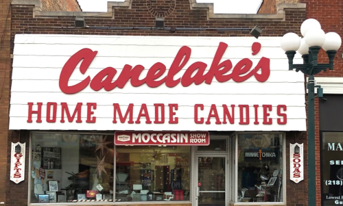 Sign for Canelake's Home Made Candies, featuring a storefront with gifts, sodas, and a moccasin show room.