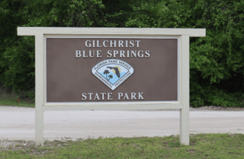 Sign for Gilchrist Blue Springs State Park, featuring the Florida Park Service logo and surrounded by greenery.