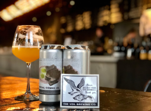 A glass of orange beer next to two cans and a sign reading "Please do not feed the animals. Thank you."