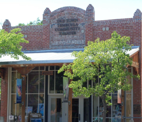 Historic brick building with a sign reading "Dale Edwin Community Center," featuring trees and a welcoming entrance.