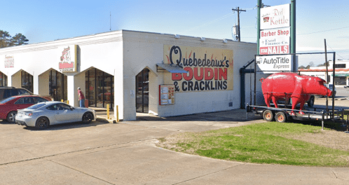 A storefront featuring "Quebedeaux's Boudin & Cracklins" with a red pig statue outside and nearby businesses.