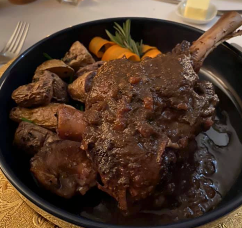 A hearty dish featuring a large, sauced meat joint with roasted potatoes and garnished with herbs and vegetables.