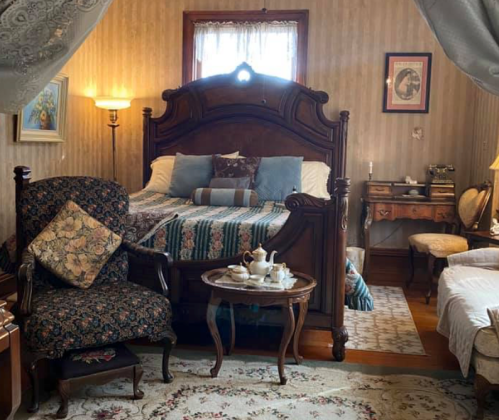 Cozy vintage bedroom with a wooden bed, floral armchair, small table with tea set, and elegant decor.
