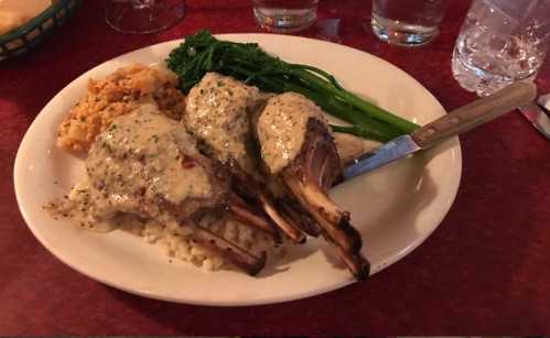 Plate of three lamb chops with creamy sauce, served with rice, broccolini, and a side of mashed potatoes.