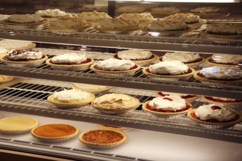 A display case filled with various pies topped with whipped cream, including fruit and custard varieties.