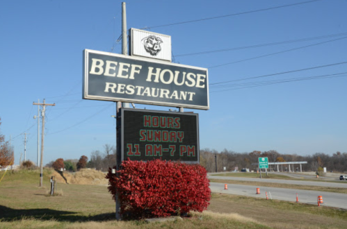 Sign for Beef House Restaurant displaying hours: Sunday 11 AM - 7 PM, with a backdrop of autumn foliage.
