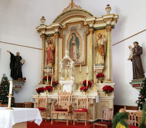 Altar in a church featuring religious statues, floral decorations, and a central image of the Virgin Mary.