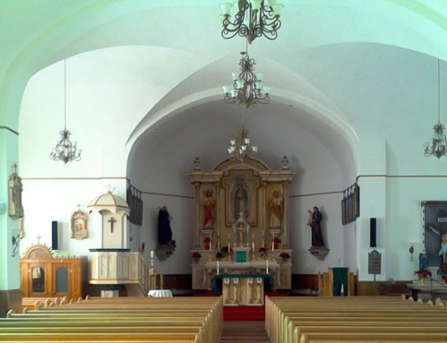 Interior of a church featuring wooden pews, an altar with religious statues, and ornate chandeliers.