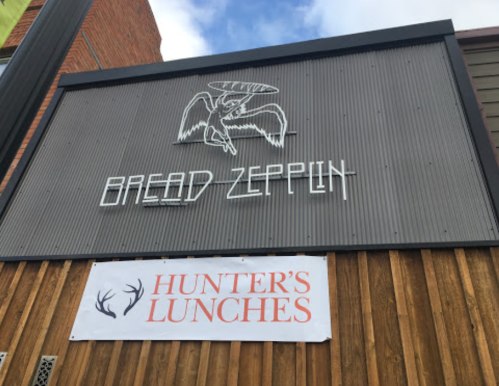 Sign for "Bread Zeppelin" with a graphic of a flying creature, below a banner for "Hunter's Lunches."