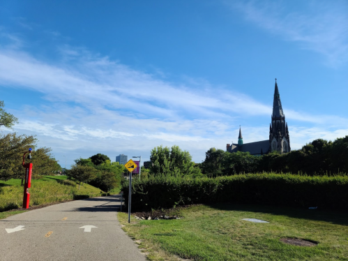 A pathway leads to a church with a tall spire, surrounded by greenery and a clear blue sky.