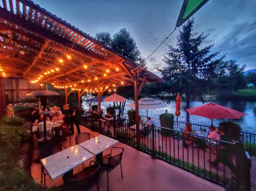 Cozy outdoor dining area by a lake, with string lights, umbrellas, and guests enjoying the evening ambiance.