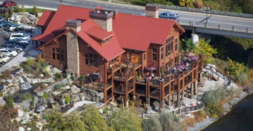 Aerial view of a large wooden lodge with a red roof, surrounded by greenery and a parking lot nearby.