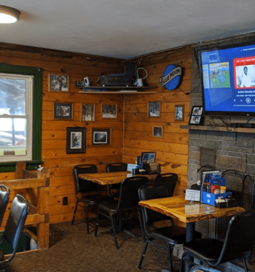 Cozy restaurant interior with wooden walls, tables, and a TV displaying music. Photos adorn the walls.