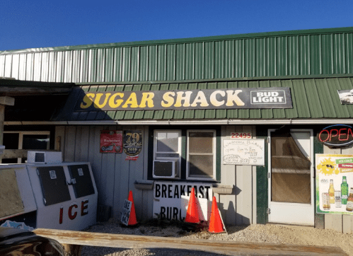 Exterior of a building with a sign reading "Sugar Shack," featuring an open sign and a menu for breakfast burritos.