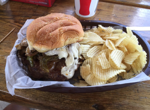 A juicy burger with onions and mayo, served with a side of crispy potato chips in a wooden basket.