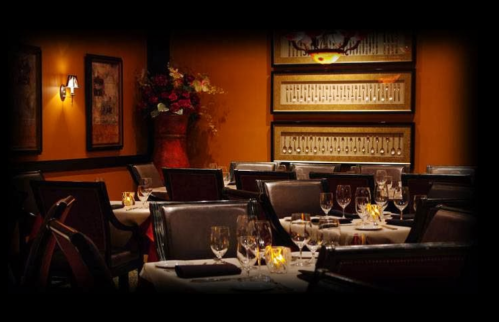 Elegant restaurant interior with tables set for dining, warm lighting, and decorative floral arrangements.
