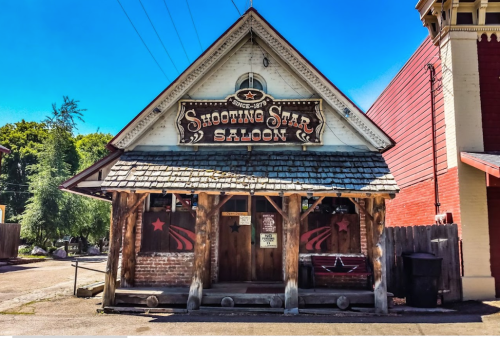 A rustic saloon with a wooden facade and a sign reading "Shooting Star Saloon" under a clear blue sky.