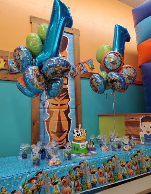 A colorful birthday party setup with balloons, a cake, and treats on a table decorated with a cartoon theme.