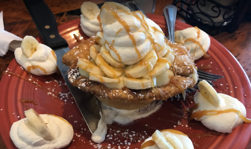A dessert featuring a pie topped with whipped cream, banana slices, and caramel sauce, surrounded by dollops of whipped cream.