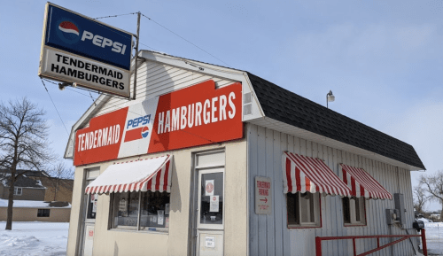 A small, retro-style fast food building with a red and white striped awning, featuring signs for Tendermaid Hamburgers and Pepsi.