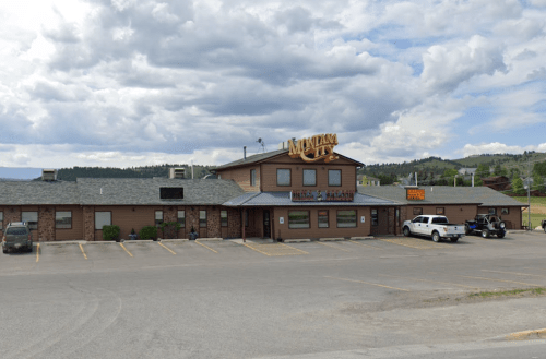 A rustic building with a sign reading "Mountain's" and parked cars in front, set against a cloudy sky.