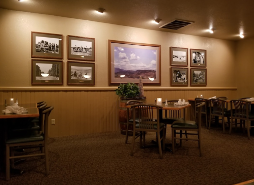 Cozy restaurant interior with wooden tables, green chairs, and framed black-and-white photos on the walls.