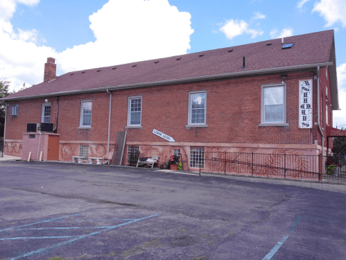 A brick building with "Antiques" sign, featuring murals and a parking lot in front under a partly cloudy sky.