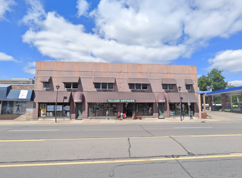 A vintage-style building with a sign reading "Village Antiques," featuring large windows and a striped awning.