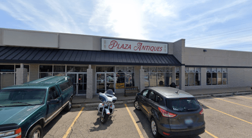 Exterior of Plaza Antiques store with parked vehicles in front and a clear blue sky above.