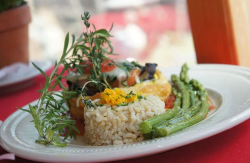 A plate of rice, asparagus, and a colorful vegetable dish garnished with fresh herbs on a red tablecloth.