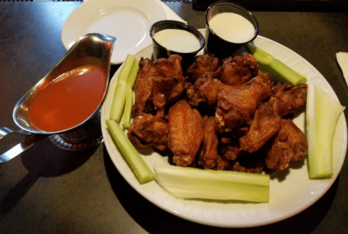 A platter of crispy chicken wings with celery sticks and two dipping sauces on the side.