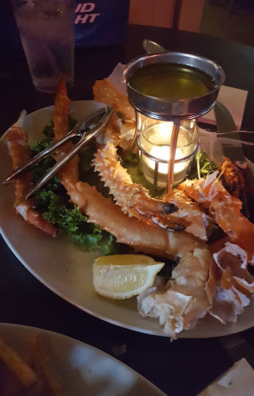 A seafood platter with crab legs, shrimp, and a candle in the center, served on a bed of lettuce with a lemon wedge.