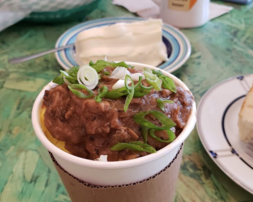 A cup of rice topped with beans and green onions, with a slice of cake and a plate in the background.