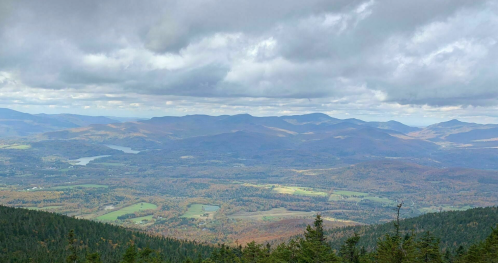 A panoramic view of rolling mountains and valleys, with autumn foliage under a cloudy sky.